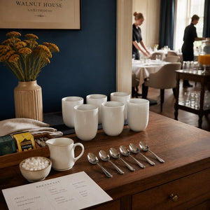 Six plain white handleless ceramic cups prepared for guesthouse breakfast service