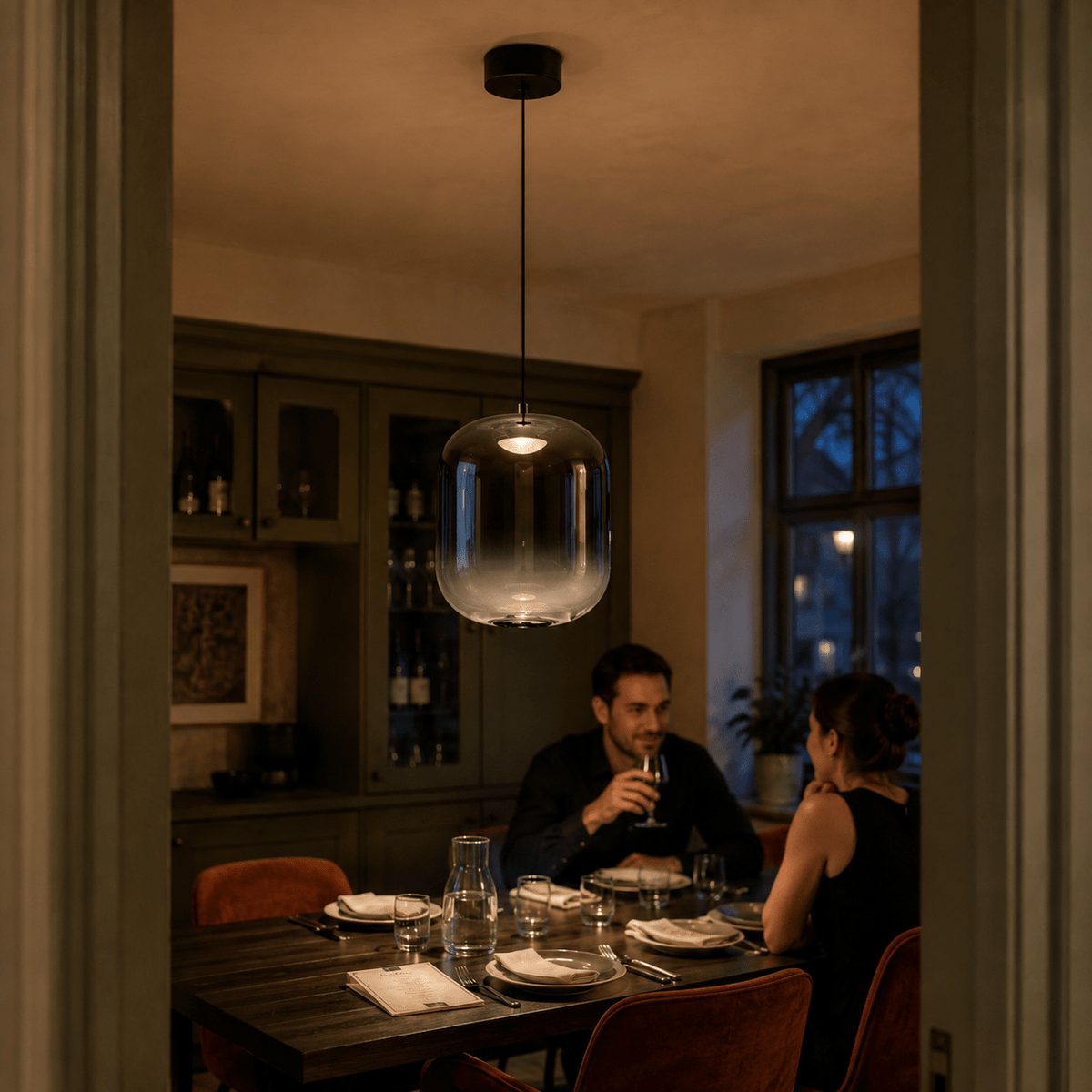 Black smoky-glass LED pendant light over an evening dining table