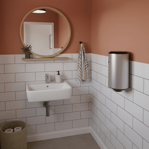 Wall-mounted stainless steel hand dryer in a tiled bathroom with a round mirror and sink.