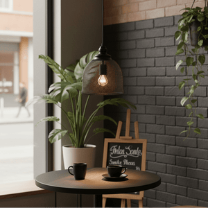 Stylish black metal pendant light hanging above a table with coffee cups, surrounded by greenery.
