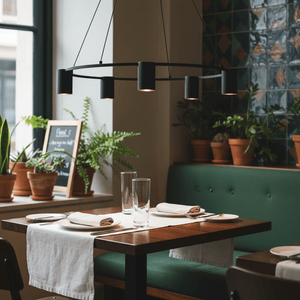 Black 5-light round pendant hanging above a dining table set with plates and glasses in a cozy restaurant.